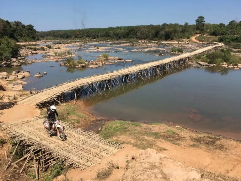 An Explore Indochina motorbike tour member crosses an enormous bamboo bridge on the Ho Chi Minh Trail in Laos