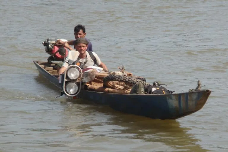 An Explore Indochina Ho Chi Minh Trail motorbike tour member crosses a river south of Muong Phin with his motorbike in a small canoe